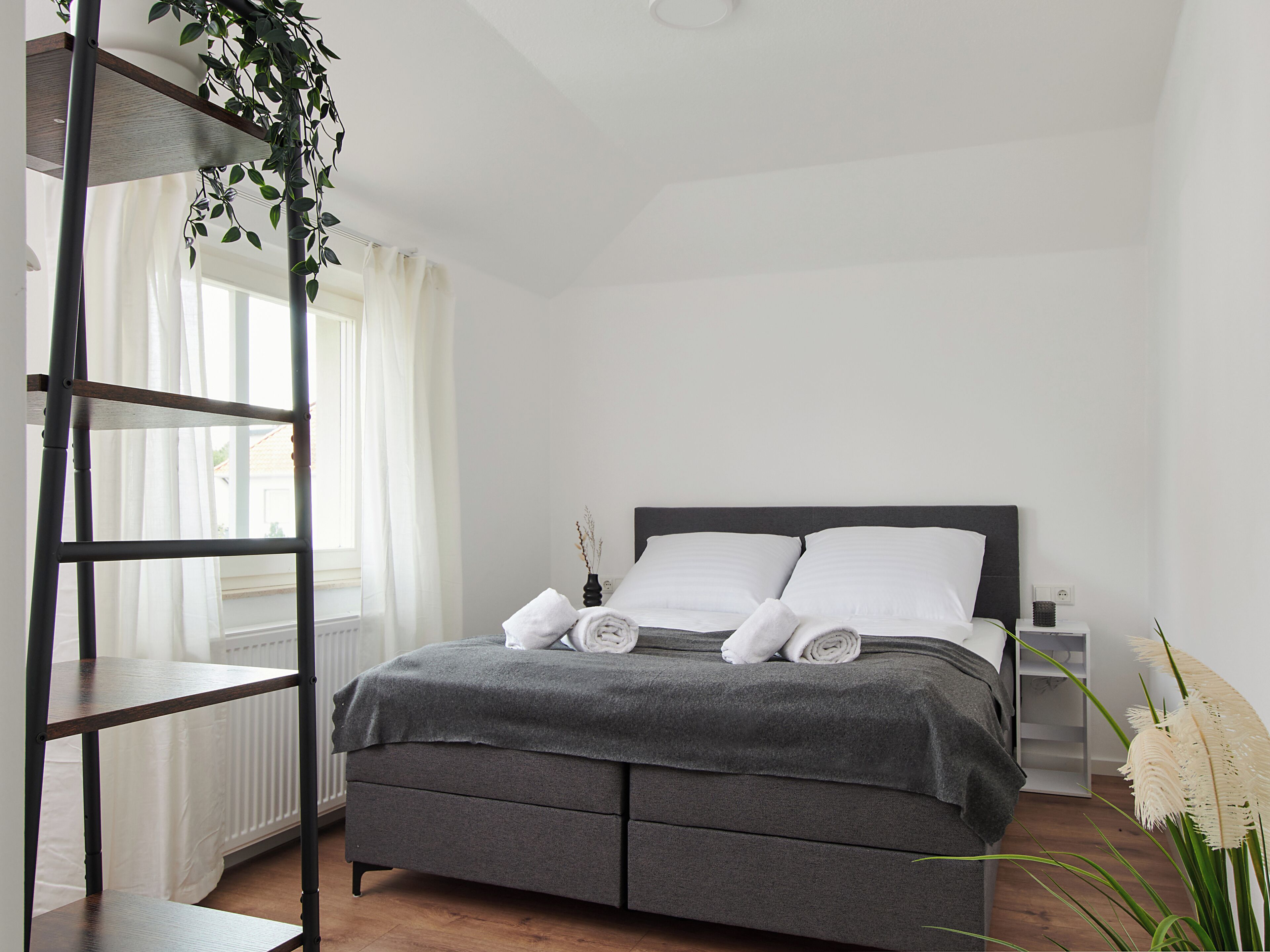 Ein Schlafzimmer mit einem Bett, einem Heizkörper, einem Nachttisch, einer Lampe und einer Pflanze.