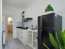 A compact kitchen with white cabinets, a black refrigerator, and a window with a plant on top.