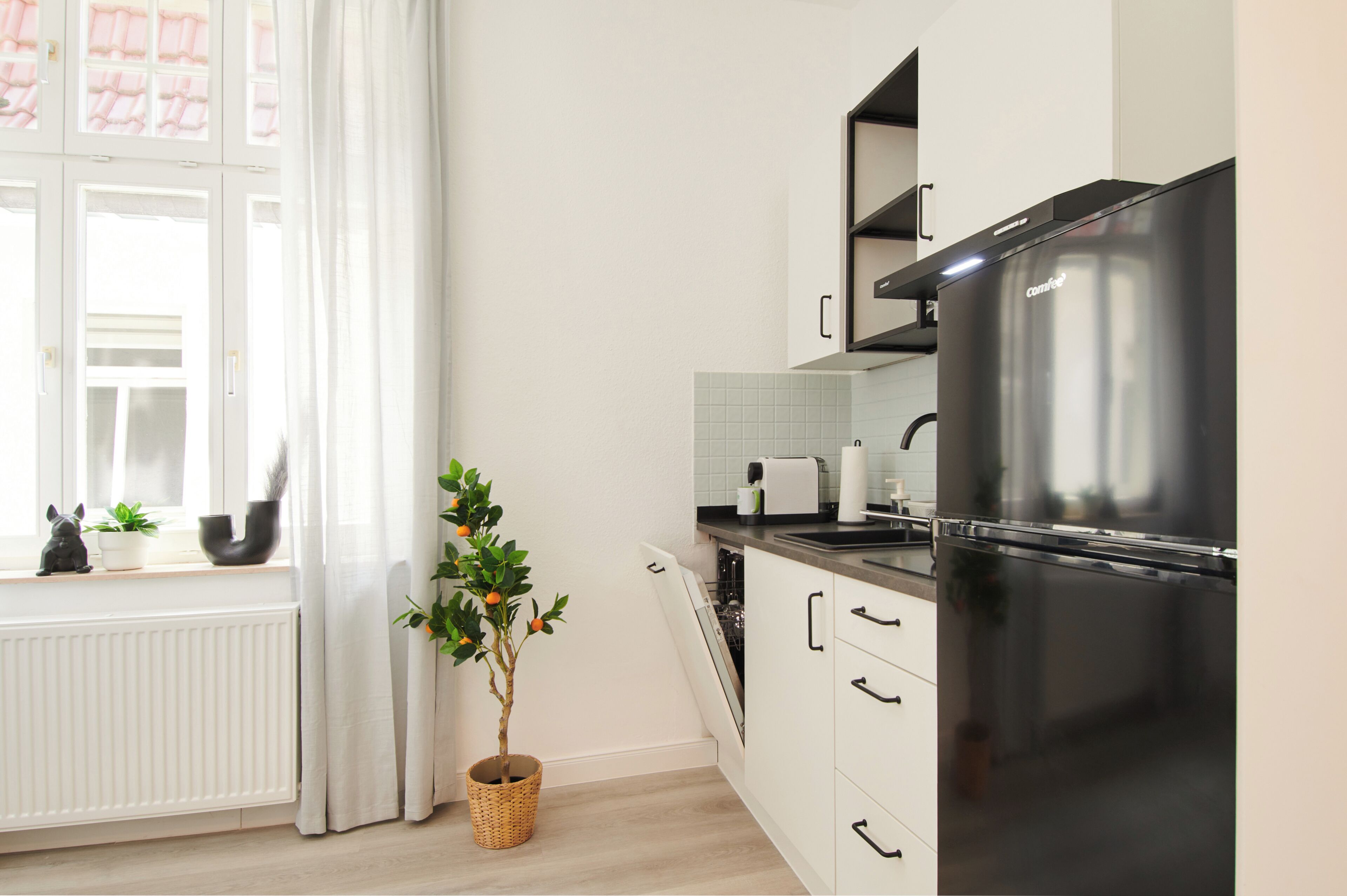 A modern kitchen with a black refrigerator, white cabinets, and a window with curtains.