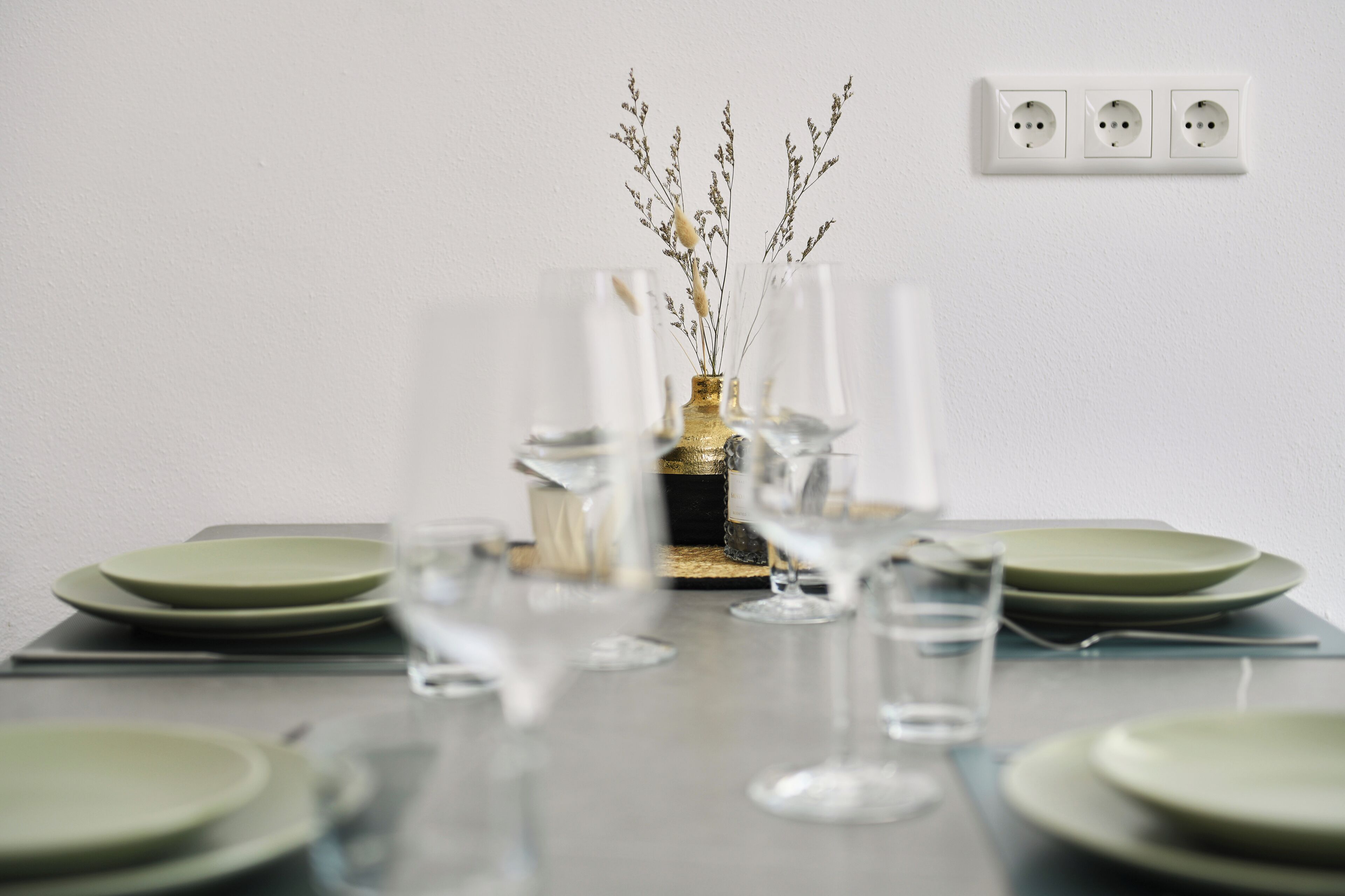 A dining table with plates, glasses, and a decorative vase with dried plants.