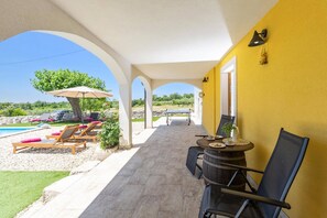 Un espacio al aire libre techado con piscina, sillas de descanso y una mesa con sillas.