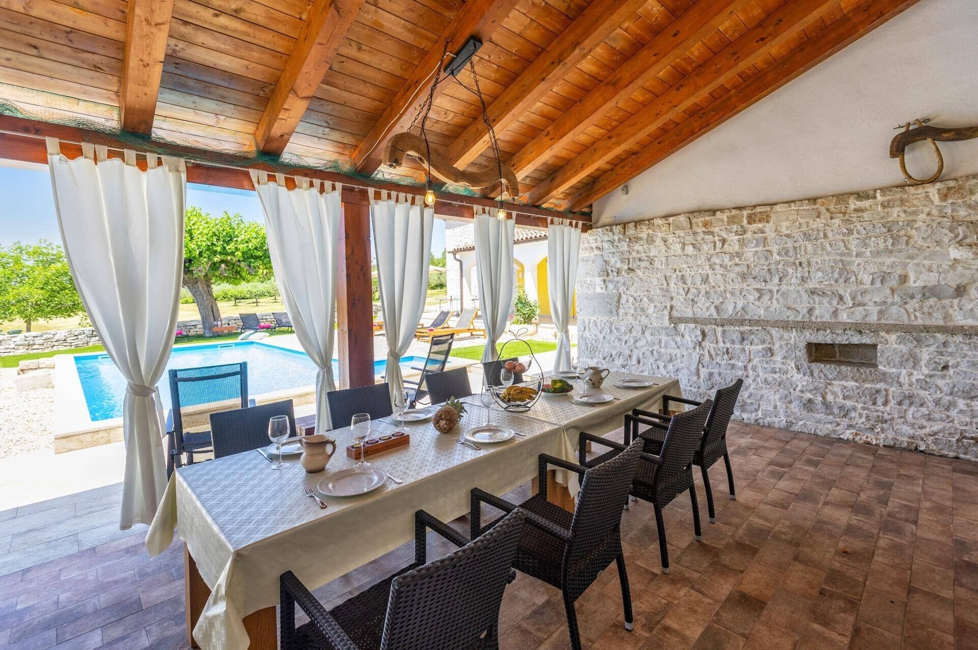 An outdoor dining area with a pool view, stone walls, and wooden beams.