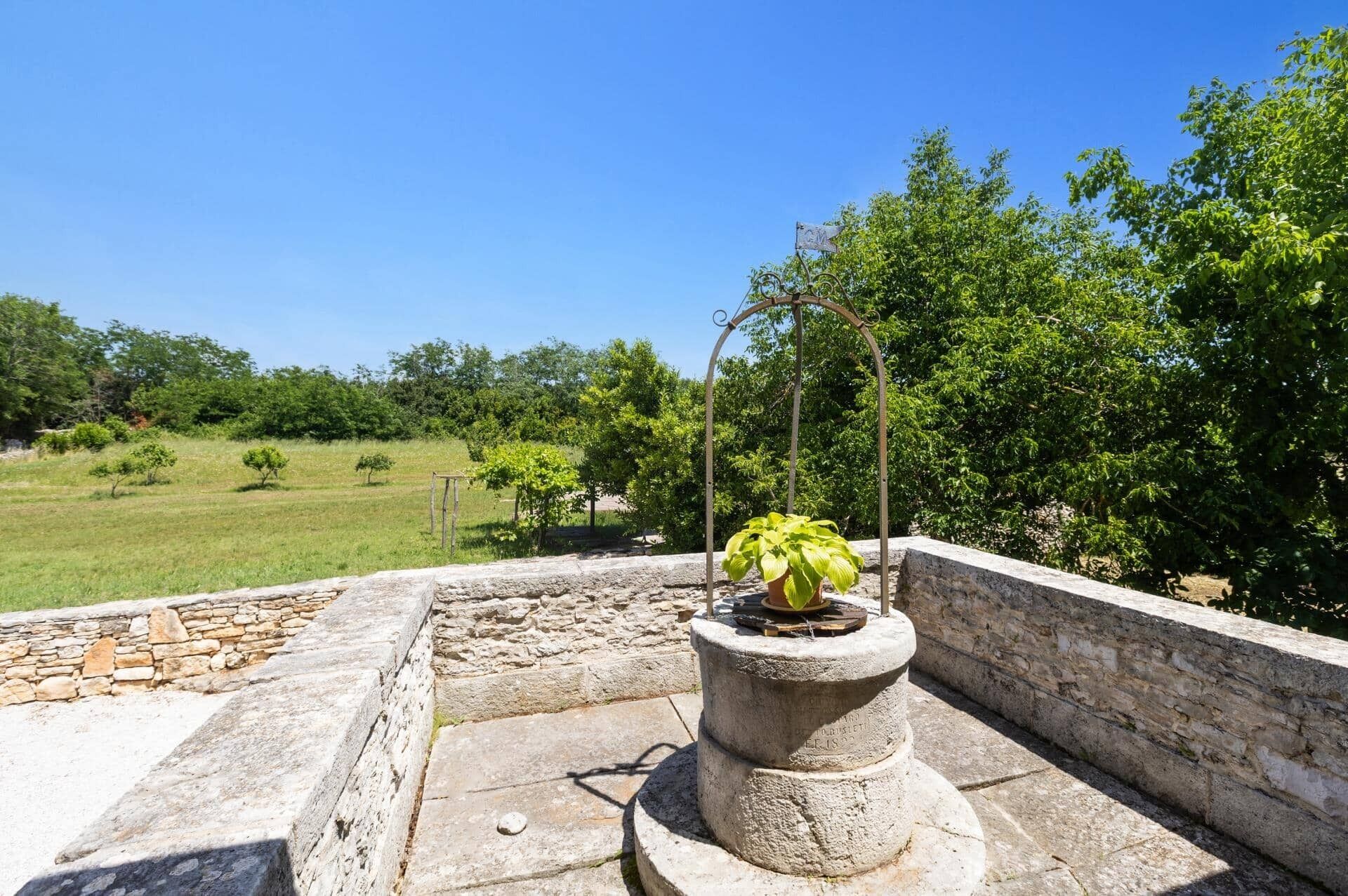 Une structure en pierre surmontée d’un pot de fleurs, entourée d’un mur de pierre et d’un champ d’herbe.