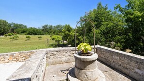 Uma estrutura de pedra com uma planta em vaso no topo, cercada por um muro de pedra e um campo gramado.