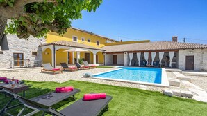 Uma área na piscina com espreguiçadeiras, uma piscina pequena e um edifício de pedra com telhado em azulejos.