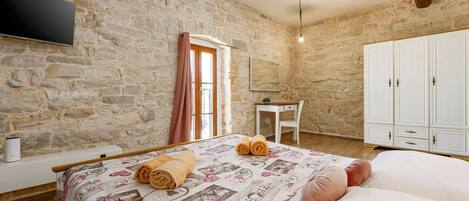 Une chambre avec un mur en pierre, un lit avec des serviettes roulées, un bureau et une armoire.