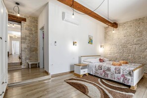 Une chambre avec un mur en pierre, un lit recouvert d’une couvre-lit à motifs, une table de chevet et une petite table de nuit.