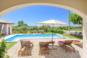 Un área de piscina con una piscina azul cristalina, rodeada de guijarros, y equipada con sillas de descanso y una sombrilla.