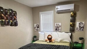 Un dormitori amb un llit, aire condicionat fixat a la paret, una finestra amb persianes i una pared decorada amb temàtica animal.