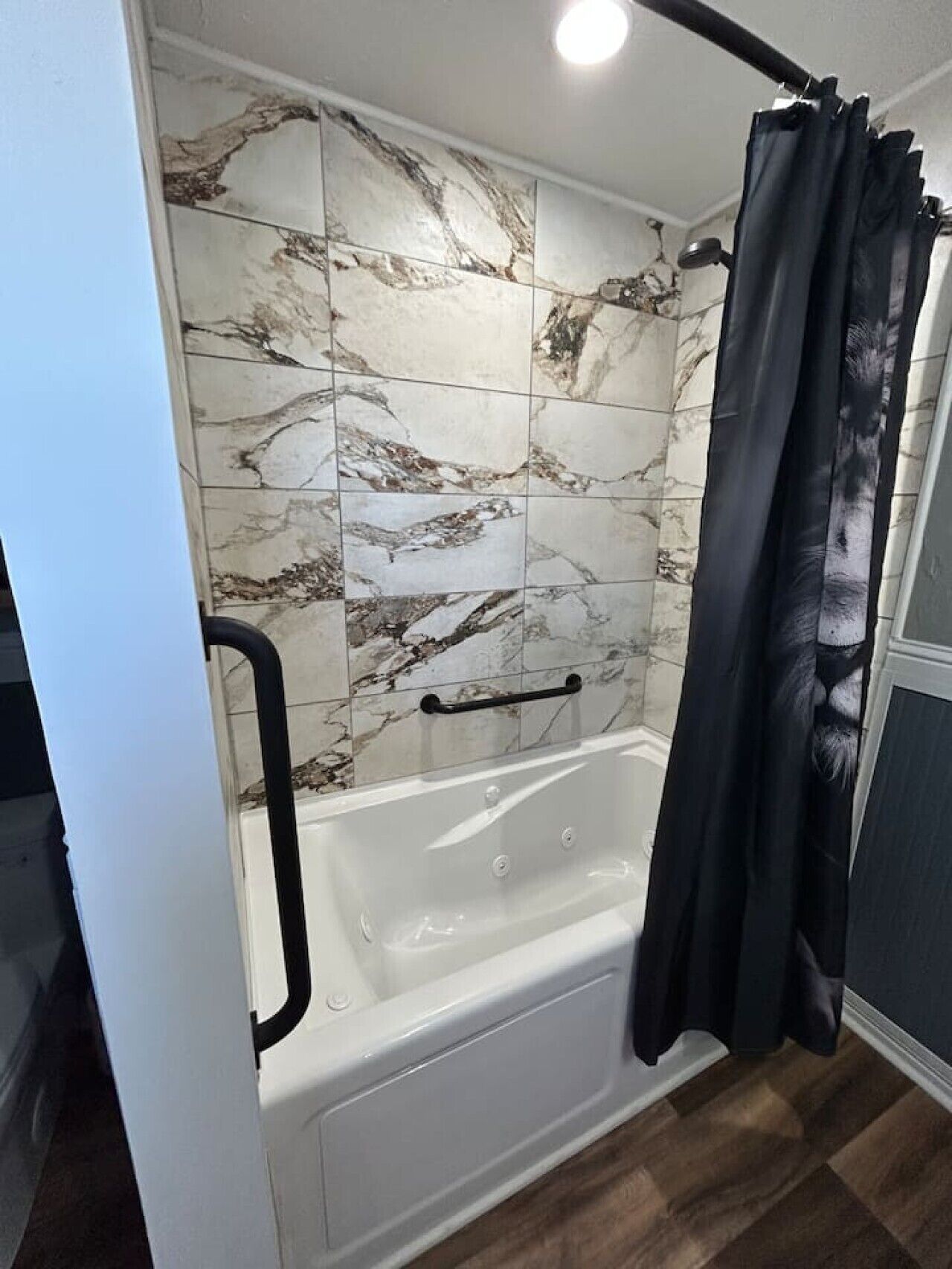 A bathroom with a bathtub, a shower curtain, and marble-patterned tiles.