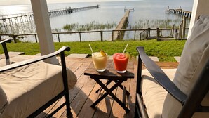 A wooden deck with two chairs and a table, overlooking a body of water and a pier. - Copano Bay Waterfront Cottage with 300 Ft Fishing Pier, sleeps 8, Pets Ok (Bayside)