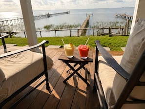 A wooden deck with two chairs and a table, overlooking a body of water and a pier. - Copano Bay Waterfront Cottage with 300 Ft Fishing Pier, sleeps 8, Pets Ok (Bayside)