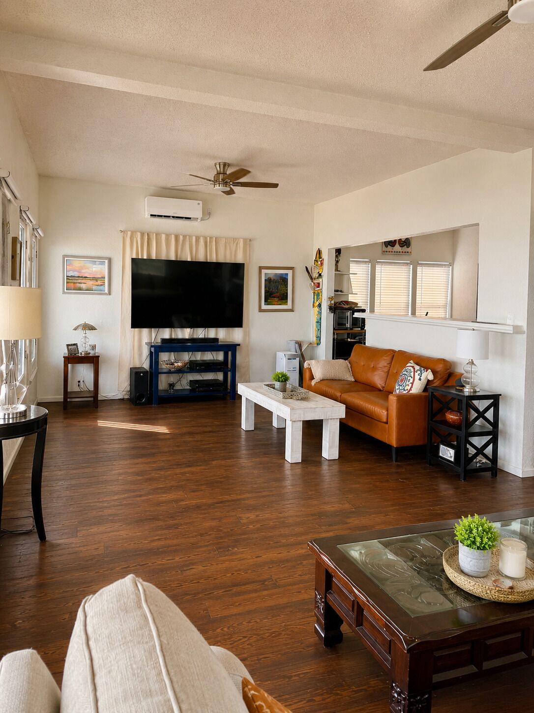 A living room with a flat-screen TV, a ceiling fan, a sofa, a coffee table, and a glass-top coffee table with decorative items.