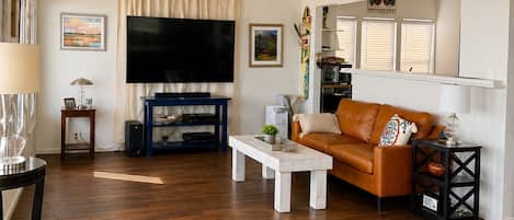 A living room with a flat-screen TV, a ceiling fan, a sofa, a coffee table, and a glass-top coffee table with decorative items.