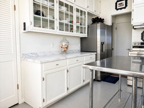 Une cuisine avec des meubles blancs, un plan de travail en marbre, un réfrigérateur en acier inoxydable et une cuisinière à gaz.