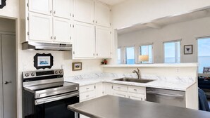 A modern kitchen with white cabinets, stainless steel appliances, and a view of the sea through large windows. - Copano Bay Waterfront Cottage with 300 Ft Fishing Pier, sleeps 8, Pets Ok (Bayside)