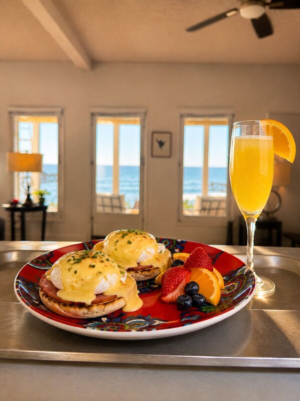 Ein Frühstückstisch mit Eggs Benedict, Erdbeeren, Blaubeeren und einer Orangenscheibe auf einem Teller, dazu ein Glas Orangensaft.