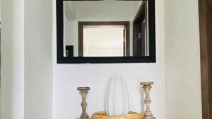 A hallway with a mirror, a white vase, and a wooden shelf with decorative items. - New Kingston Comfy 2BR Apartment  (Kingston)