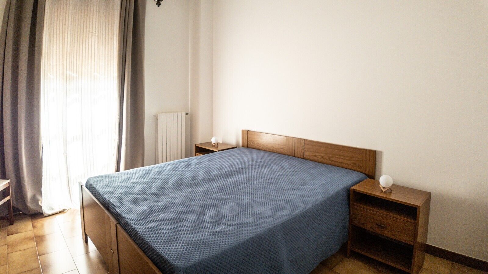 A bedroom with a bed, wooden headboard, bedside tables, and a radiator.