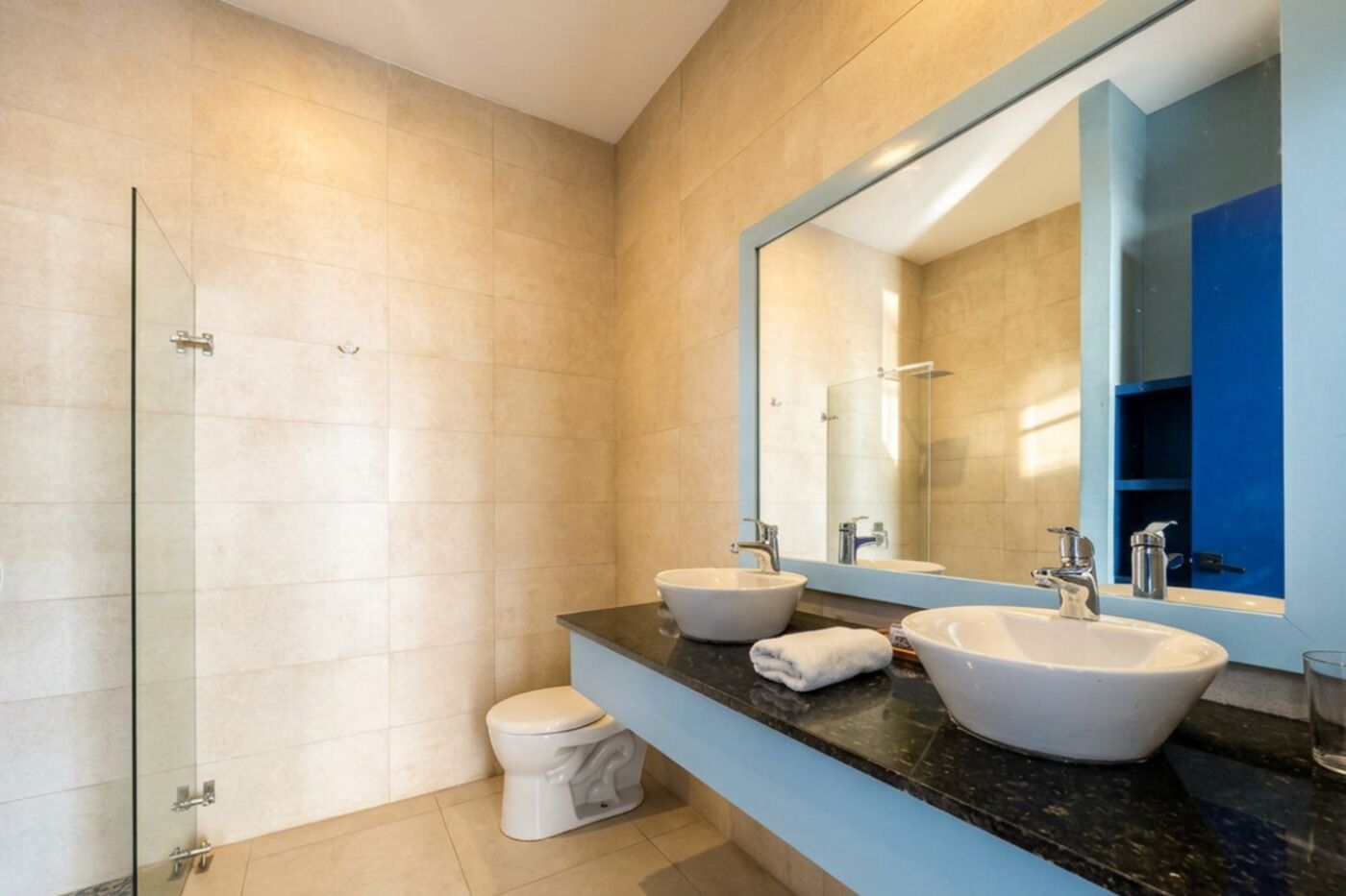 A modern bathroom with a glass shower enclosure, a toilet, and two sinks with a large mirror above.