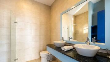 A modern bathroom with a glass shower enclosure, a toilet, and two sinks with a large mirror above.