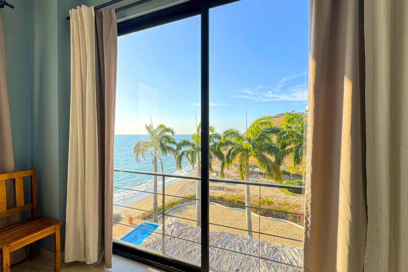 A room with a large window overlooking a beach with palm trees and a clear sky.