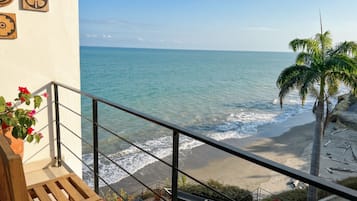 A balcony with a view of the ocean, a palm tree, and a railing.