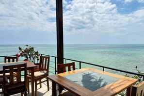 Una terraza de madera con una mesa y sillas frente a un mar azul y transparente.