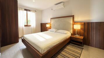 Quarto de hotel com cama grande, luminárias de cabeceira, ar condicionado e janela com cortinas.