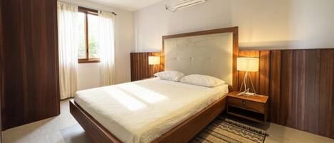 Una habitación de hotel con una cama grande, lámparas de noche, un equipo de aire acondicionado y una ventana con cortinas.