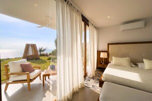 A hotel room with a balcony, a bed, a chair, a nightstand, and a view of the sea.