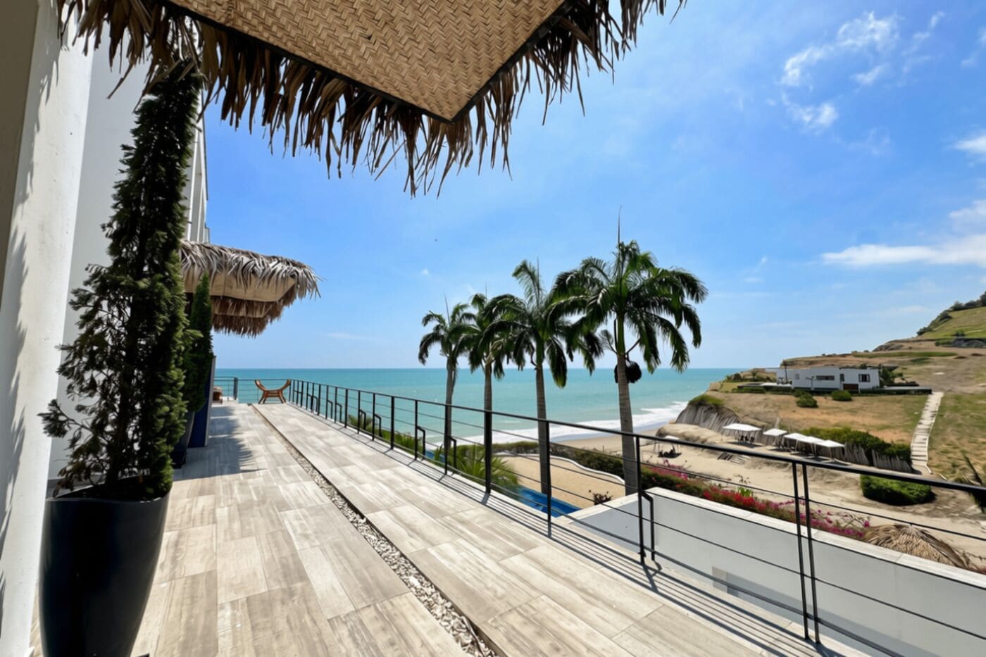 A balcony with a view of the beach, palm trees, and a white building.