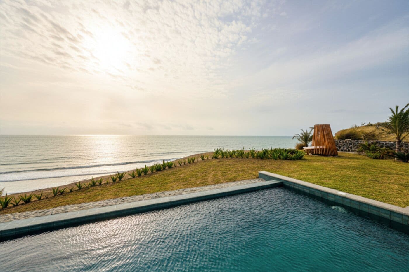 A swimming pool with a view of the ocean and a beach area with a lounge chair.