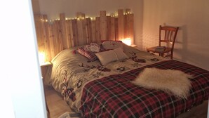 A bedroom with a bed, a chair, a shelf with decorative items, and a wall-mounted picture. - APARTMENT NEAR LUZ SAINT SAUVEUR 4/5 -PERSON APARTMENT (Esquièze-Sère)