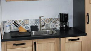 A kitchen with wooden cabinets, a black countertop, a stainless steel sink, a coffee maker, and a microwave. - APARTMENT NEAR LUZ SAINT SAUVEUR 4/5 -PERSON APARTMENT (Esquièze-Sère)