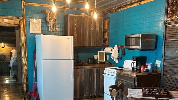 A compact kitchen with a refrigerator, stove, microwave, and a dining area with a table and chairs. - Western cabin in Blanchard, OK (Blanchard)