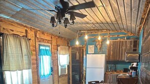 A cozy cabin interior with a sofa, wooden walls, a ceiling fan, and a kitchenette. - Western cabin in Blanchard, OK (Blanchard)