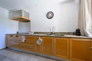 Una cocina con armarios de madera, una campana extractora de acero inoxidable, un fregadero y un reloj en la pared.