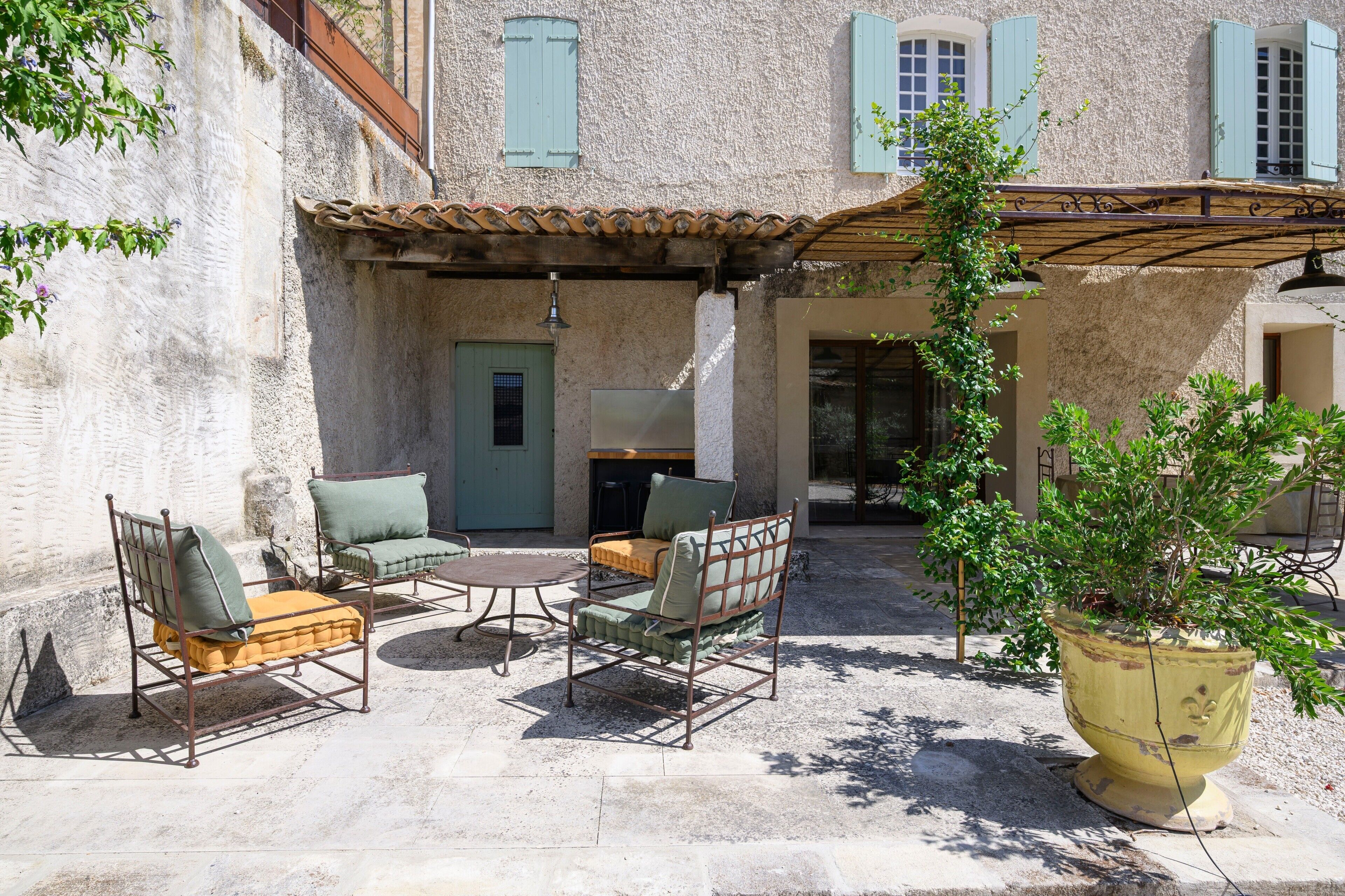 An outdoor patio with metal furniture, a yellow planter, and a building with stone walls and blue shutters.
