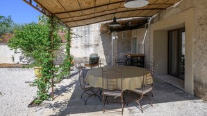 Un patio al aire libre con una mesa redonda y sillas, un colgante de luz y una pérgola.