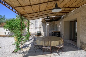 An outdoor patio with a round table and chairs, a hanging light fixture, and a pergola overhead.