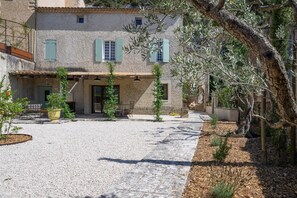 A courtyard with a stone building, outdoor seating, and olive trees.