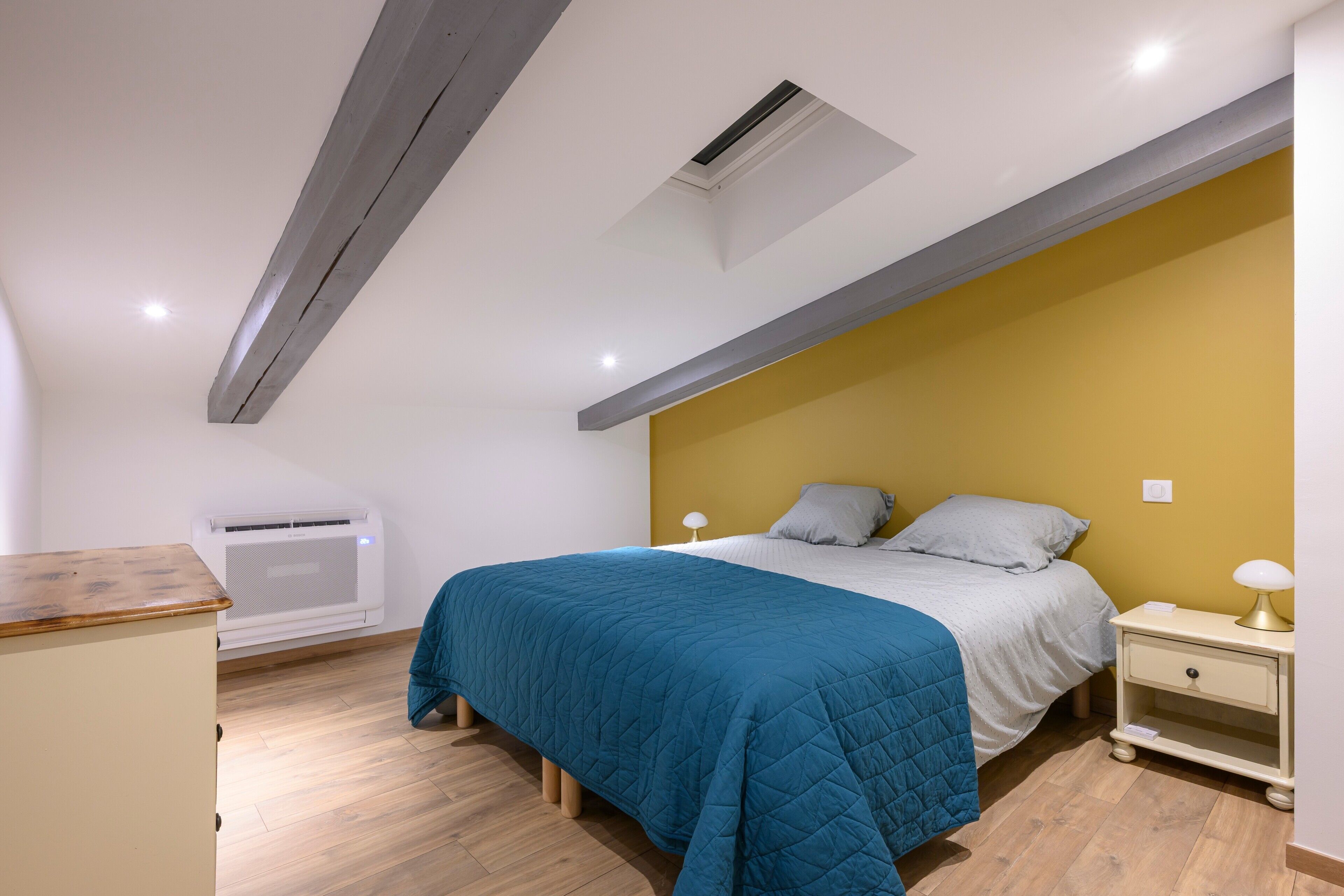 Un dormitorio con cama, mesitas de noche, aire acondicionado y piso de madera.