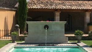 Una piscina con una fuente de agua, rodeada por un muro de piedra y plantas en macetas.