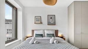 A hotel room with a bed, two pillows, a framed artwork, a nightstand, a bedside lamp, and a wardrobe. - Scandi & Modern Apartment in Heart of Bratislava (Bratislava I)