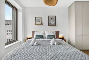 A hotel room with a bed, two pillows, a framed artwork, a nightstand, a bedside lamp, and a wardrobe. - Scandi & Modern Apartment in Heart of Bratislava (Bratislava I)