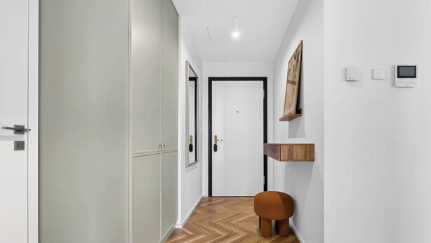 A hallway with a wooden floor, a white door, a small stool, and a wall-mounted shelf with a picture. - Scandi & Modern Apartment in Heart of Bratislava (Bratislava I)