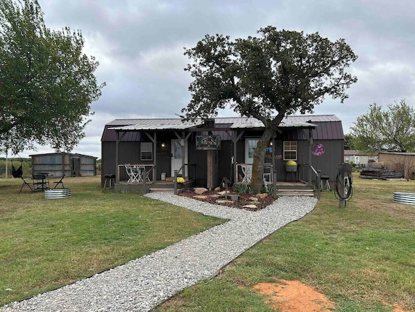 A rustic building with a porch, a tree in front, and a gravel pathway leading to the entrance.