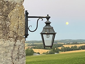 A street lamp attached to a stone wall, overlooking a rural landscape with fields and distant hills.