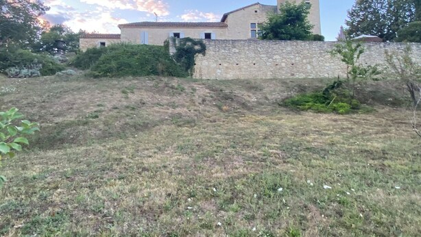En bygning i sten med et tårn, omgivet af en stenvæg og vegetation.